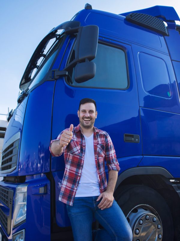 Professional truck driver in front of long transportation vehicle holding thumbs up ready for a new ride.